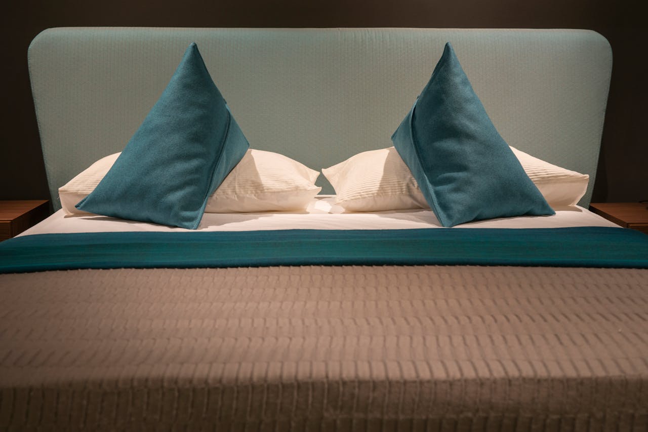 Modern minimalist bed with teal pillows and headboard, showcasing elegant interior design.